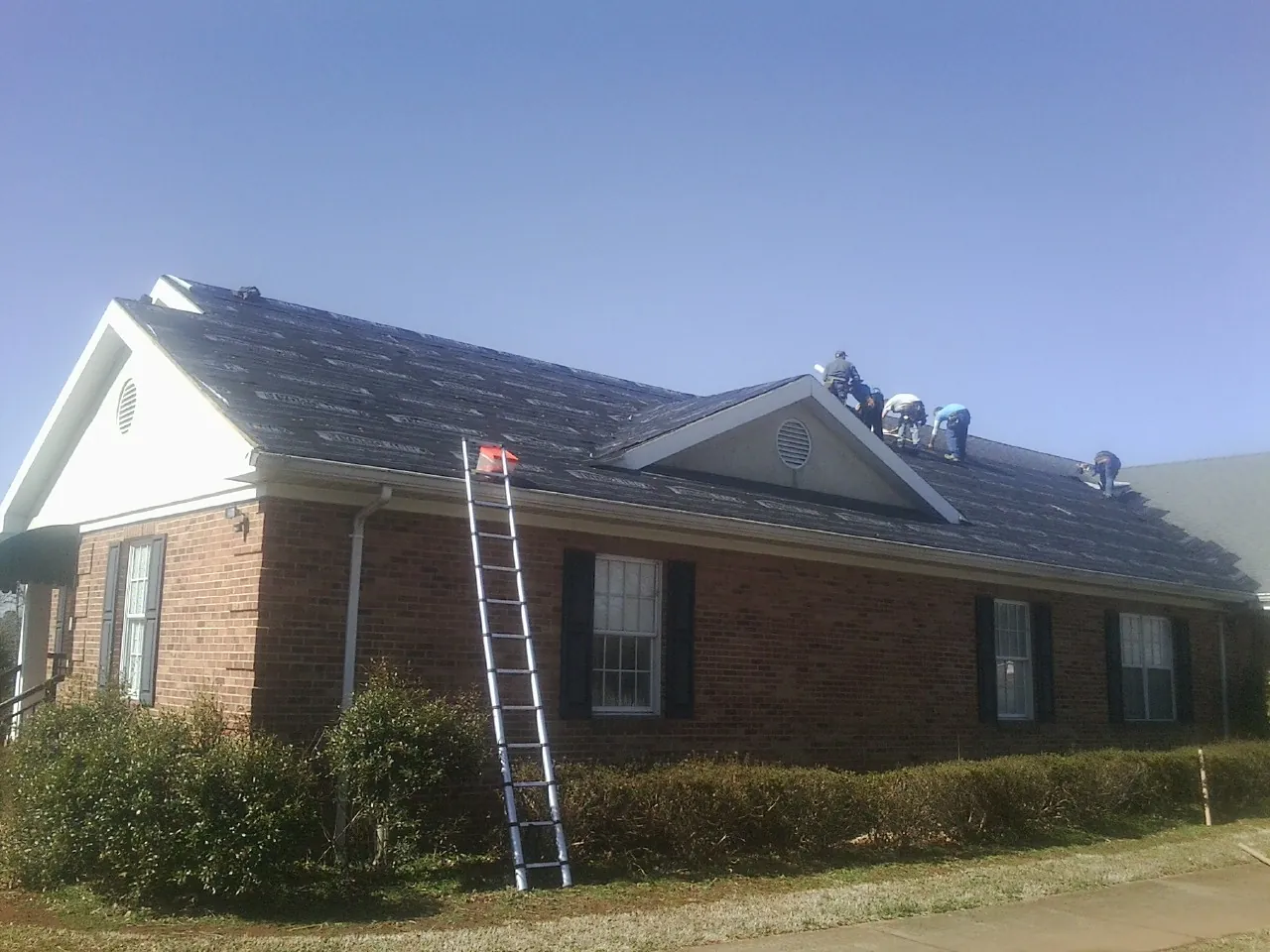 Crew tearing shingles off a brick ranch roof with a ladder set — Metal Roof Repair work by our crew in Amelia Court House