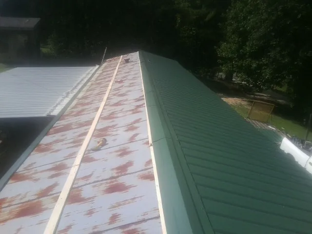 Old rusted panels beside newly installed green metal roofing — Wind Damage Roof Repair by Roofing Brothers in Amelia Court House