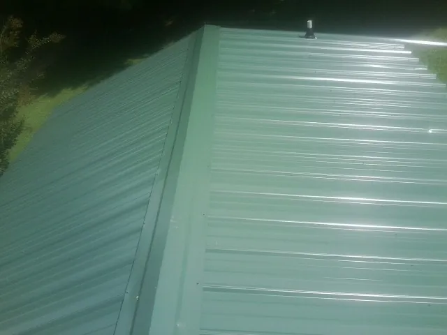 New green metal panels meeting at the ridge of a roof — Flat Roof Repair work by our crew in Amelia Court House
