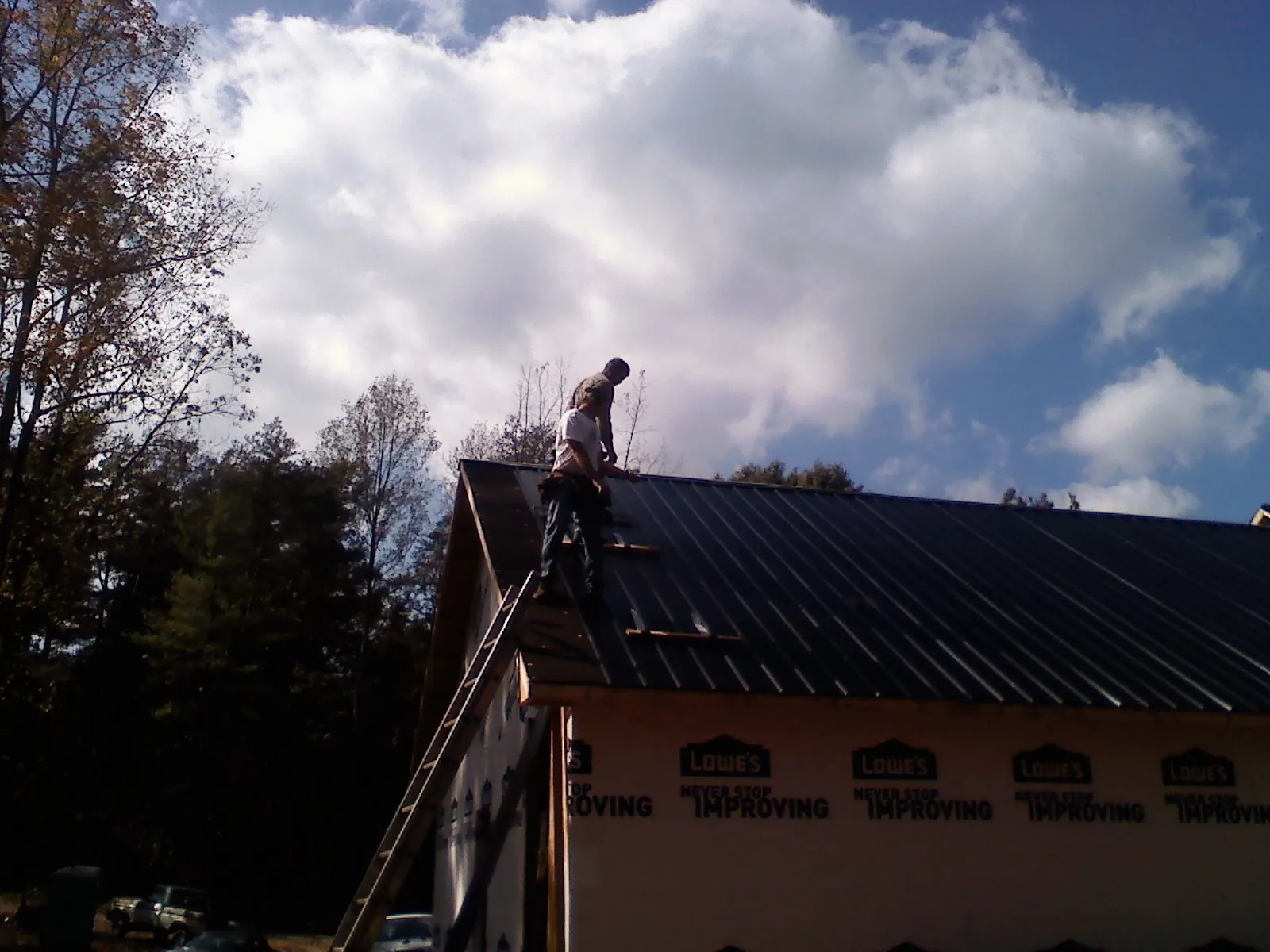 Roofer fastening dark metal panels high against a cloudy sky, from a Roof Inspection job in Amelia Court House