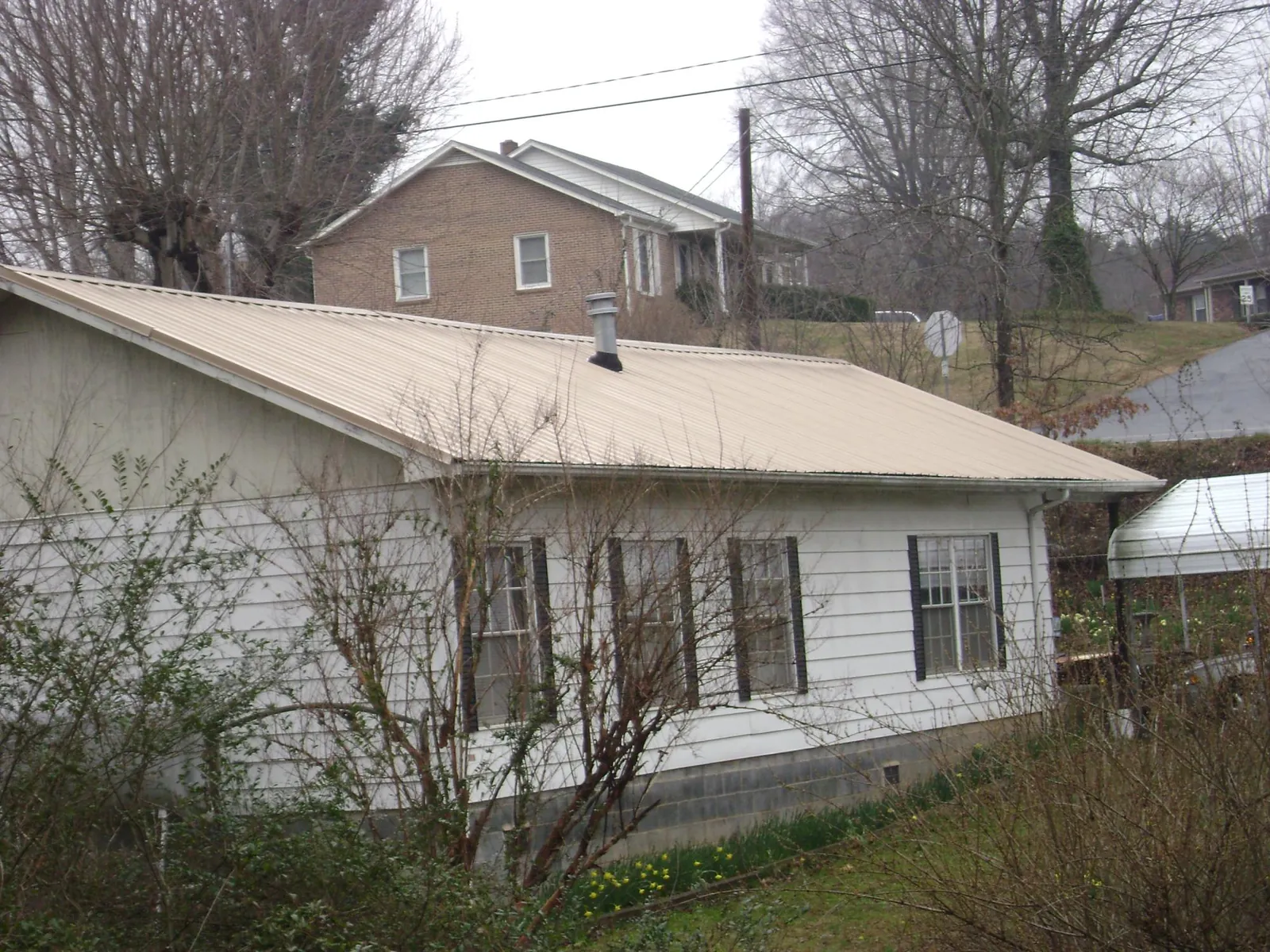 Tan metal roof on a white sided house set into a hillside — Commercial Roofing by Roofing Brothers in Amelia Court House